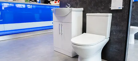 Modern white toilet and compact sink vanity unit on display in a Plumb Centre bathroom showroom.