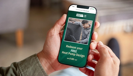 A phone with an image of a man stood infront of a heat pump, and the words: redeem your FREE Heat Pump Design
